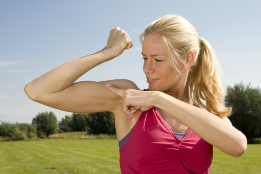 Blondýnka v červeném sportovním topu ukazuje a ukazuje na bicepsy 