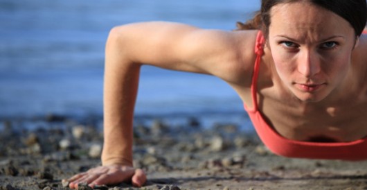Fit girl is doing push ups on the beach and looking into the camera