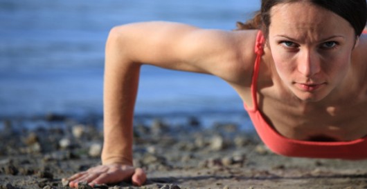 Una chica en forma hace flexiones en la playa y mira a la cámara