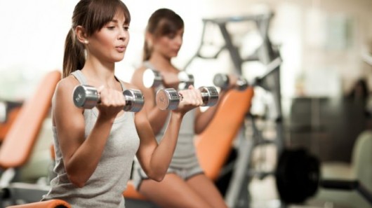 Entrenamiento con pesas para la parte superior de los brazos. Chica está haciendo curl con mancuernas en el gimnasio. Ella está entrenando sus brazos