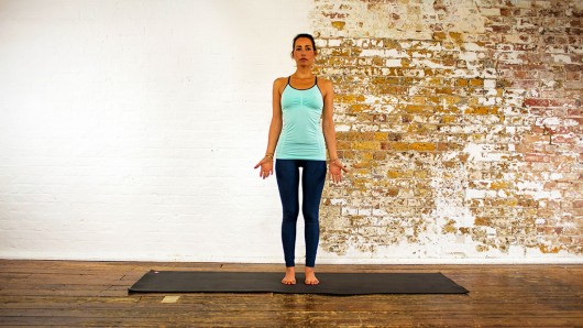 The girl is standing on the mat with her palms turned and doing Mountain Pose