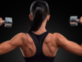 Girl standing with her back with dumbbells in each hand and showing her beautiful shoulders and arms