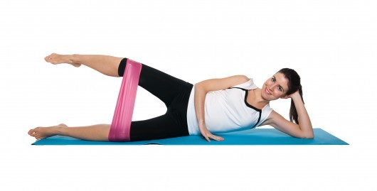 Fit girl on white lying on the mat and doing resistance band workout