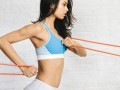 A fit and beautiful girl in a blue sporty top on the white background doing full body resistance band workout