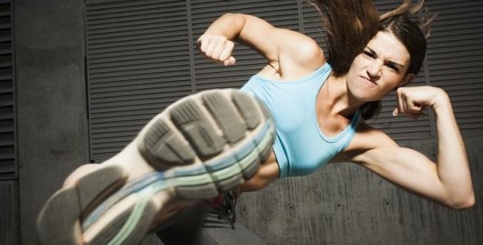 A strong and beautiful girl on the grey background does front kick with her leg showing the sole of the shoe