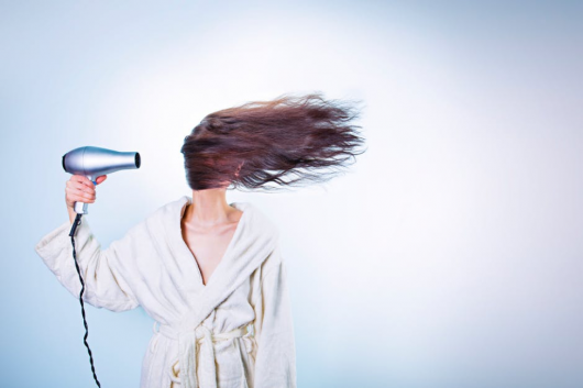 Girl in a white wardrobe on the white background drying her hair so her hair is all around her face