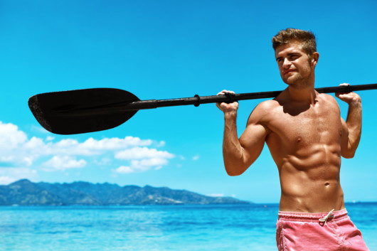 Handsome Athletic Man With Sexy body In swimwear holding canoe kayak paddle on the beach. A fit and sexy man is showing his strong body and holding kayak paddle