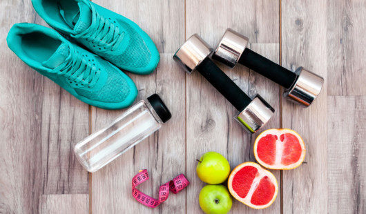 Running shoes, dumbbells, water bottle and fruit are on the wooden background