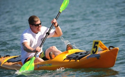 Guy in a white t-shirt and black sunglasses paddling in the yellow kayak
