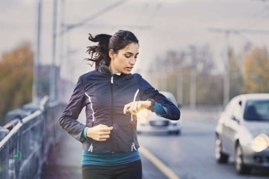 A young woman is checking her fitness watches while jogging along the road