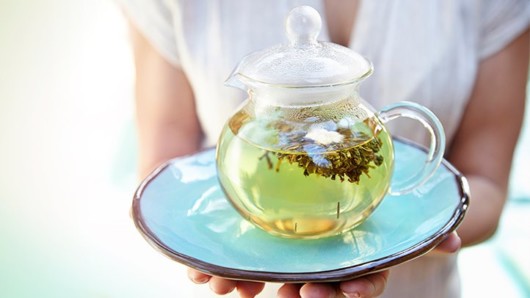 a girl holds a plate with a a transparent teapot full of green tea