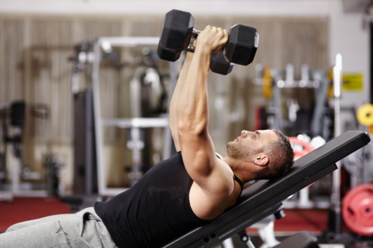 A guy is exercising with dumbbells on the bench in the gym 