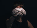 A woman in black and on black background is holding the plastic brain in front of her