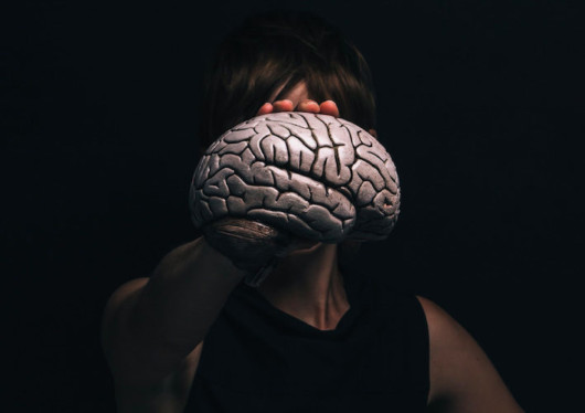 A woman in black and on black background is holding the plastic brain in front of her