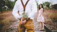 A romantic guy with flowers behind his back and the girl stands in front of him. they are both outside