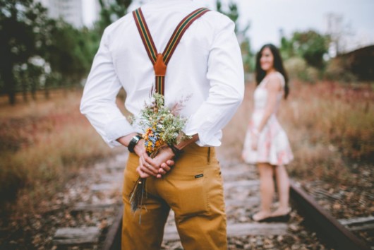 A romantic guy with flowers behind his back and the girl stands in front of him. they are both outside