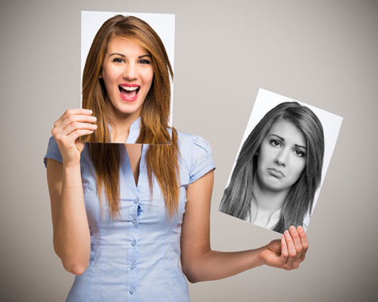 A girl with a happy and sad pictures of herself on grey