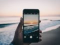 A close up sell phone with beautiful see and sunset on the screen and at the background