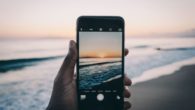 A close up sell phone with beautiful see and sunset on the screen and at the background