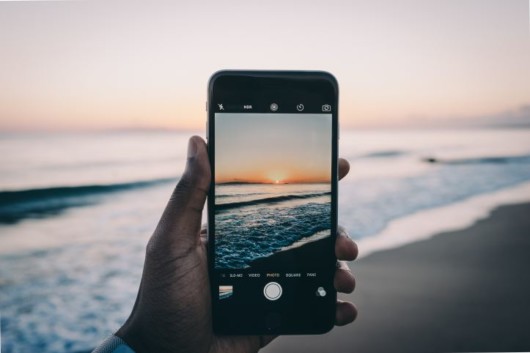 A close up sell phone with beautiful see and sunset on the screen and at the background