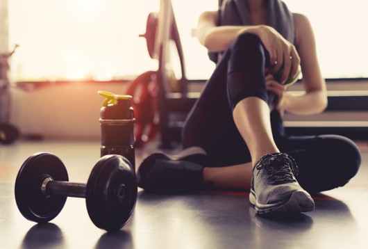 Girl is sitting in the gym with dumbbell and bottle of water