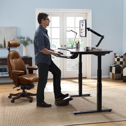 A guy is standing and working at sit-stand converter table in the home office