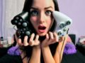 A girl is holding two gamepads close to her face and opens her mouth in surprise