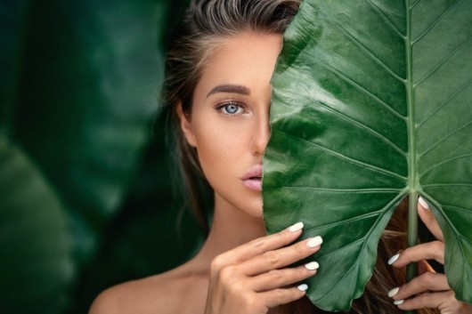 a beautiful girl is hiding her face behind the big green leaf