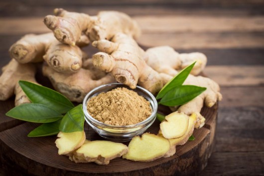 Ginger roots and ginger powder on wooden table