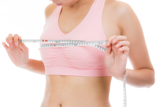 Girl in pinky sport bra is measuring her breasts with a measuring band before breast augmentation