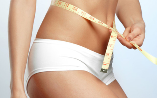 Girl on white background measuring her waist with a soft tape measure