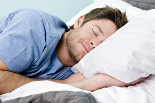 Guy in blue t-shirt slips cosy in his bed with his hands under the pillow