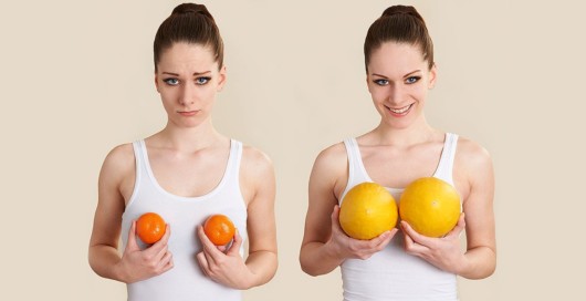 Two young girls on beige background holding small tangerines and big  oranges. Two girls imitate small and big breasts with fruits