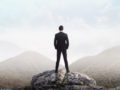 a guy in a suit stands with his back on the stone and look forward