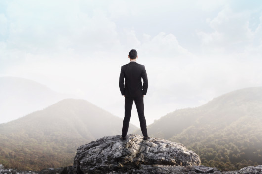 a guy in a suit stands with his back on the stone and look forward