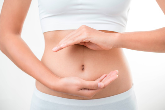 Girl on white back ground keeps her hands in front of the stomach