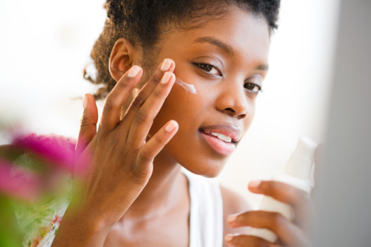 Afroamerican girl puts moisturizer on her skin as a part of skincare routine