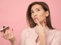 Beautiful girl on pink background is holding a cupcake in one hand and the finger in her mouth