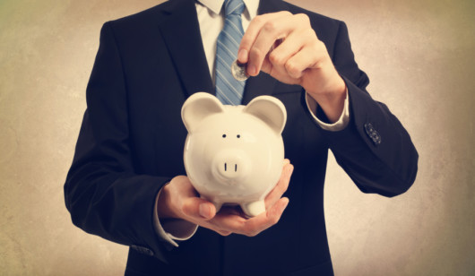 Man in a suit on brown background is collecting money into a piggy bank