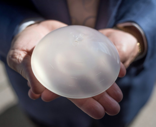 The man in holding breast implant in his hands close to the camera