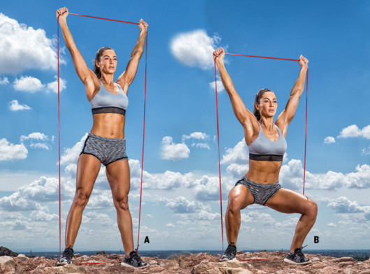 A beautiful and fit girl in sport top and shorts on the beach is doing Overhead Squats