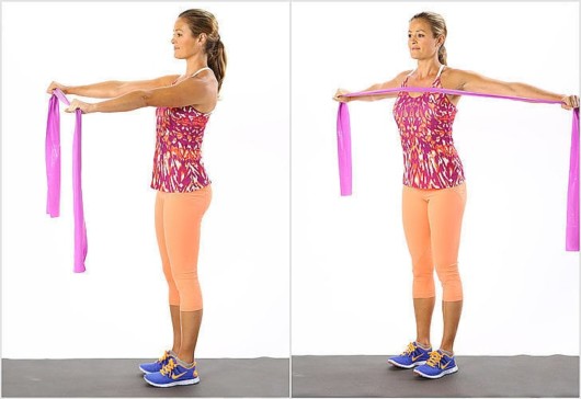 A beautiful girl in colourful sport outfit on the white background is doing Resistance Band Reverse Fly .