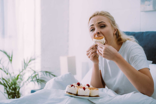 Girl eating emotionally the cakes while sitting in bed