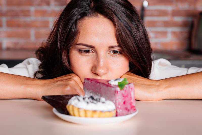 Girl is at the table and in front of the plate with cakes. She is looking at the cakes 