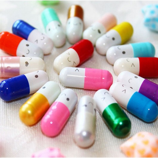 Colourful capsules with faces painted on them lying on white table