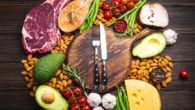 Meat, fish, avocado, greens, nuts and tomatoes with knife and fork on the wooden cutting board