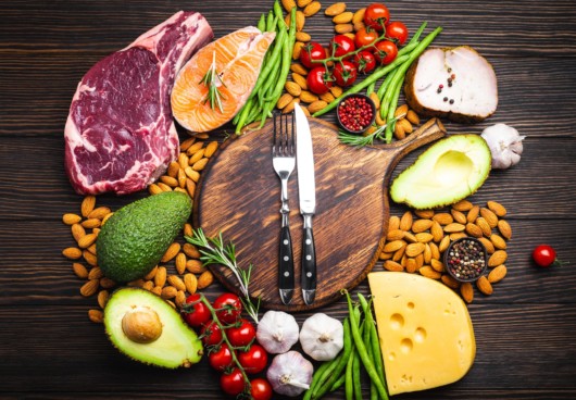 Meat, fish, avocado, greens, nuts and tomatoes with knife and fork on the wooden cutting board