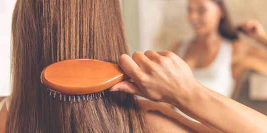 A girl is carefully brushing her dark hair in front of the mirror 