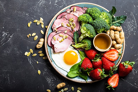 Meat, seeds, broccoli, nuts, egg and strawberries ate on the plate and dark background