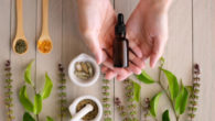 A bottle of cbd oil lies in the hands with herbs and leaves on the wooden background